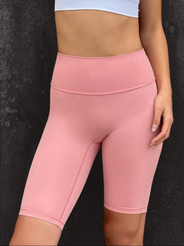 Woman wearing a whire sports bra and pink leggings against a dark textured wall.